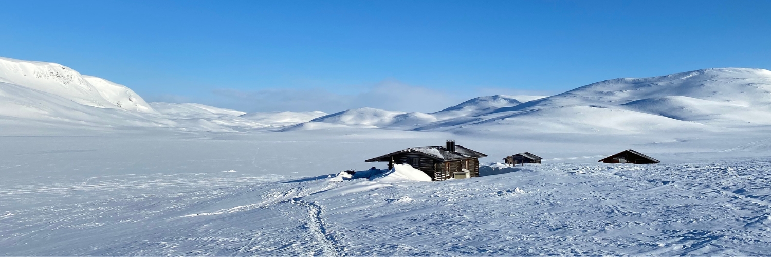 Mökki talvisessa tunturimaisemassa. Mökille johtaa latu.
